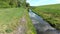 Low level flight above artificial water channel towards rusty bridge. Nice reflection of clouds present in water.