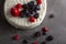 low light image of a round cake with creamy white icing and assortment of berries used as decorative toppings