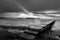 Low point view of a pier on a lake with a ray of sun against a moody sky