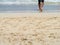 Low section of barefoot man walking into the waves on a sandy beach