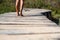 Low section legs of woman walking barefoot on elevated footbridge leading towards natural forest. Rear view of female legs moving