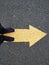 Low section of a man standing on a yellow arrow on asphalt