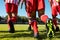 Low section of multiracial male athletes wearing red uniform and soccer shoes running on grassy land