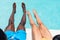 Low section of multiracial young couple dangling legs in swimming pool