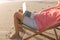 Low section of relaxed senior biracial man sitting with laptop on folding chair at beach