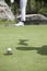 Low section of young woman hitting the ball on the golf course, focus on the hole