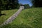 Low stone dividing wall on a hillside in an urban park, lush green landscape and blue sky