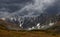 Low stormy clouds touch top of snowy mountain. Dismal overcast awesome landscape with big rocks and glacier