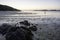 Low tide at a beach in Brittany in the evening, lonely boy walking in the shallow water, rocks in the foreground, silent dusk mood