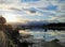 Low tide in a cove on a partly cloudy day at sunset. Calm water reflects boats, trees, shoreline