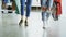 Low view of girls` legs walking slowly through spacious shop. Ladies are wearing jeans and modern trainers and carrying