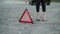 Low view of woman with broken automobile, installing red triangle sign on road