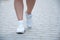 The lower part of the legs of a woman in white sneakers. Goes along the alleys in the summer
