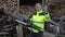 Lumberjack in reflective jacket. Man woodcutter with electric chainsaw. Show ok sign. Sawmill