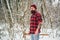 Lumberjack worker with axe in winter forest. Bearded brutal guy wears plaid shirt and knitted hat. Fashion style of hipster guy