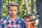 Lumberjack worker standing in the forest with chainsaw. Chainsaw. Stylish young man posing like lumberjack. Woodcutter