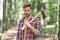 Lumbersexual man in lumberjack shirt holding axe on shoulder forest background