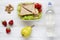 Lunch box with sandwiches, walnuts, bottle of water and fruits on white wooden table, top view. From above.