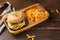 Lunch with a burger in a wooden tray, with potato chips. Dark rustic wood background, horizontal, with space