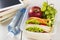 Lunchbox with sandwich, vegetables and fruit, bottle of water and pad on a white background