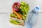 Lunchbox with sandwich, vegetables and fruit, bottle of water on a white background.