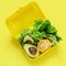 Lunchbox with a snack from lettuce, tomato, avacado on a yellow background. Healthy eating concept. Go vegan.