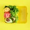 Lunchbox with a snack from lettuce, tomato, avacado on a yellow background. Healthy eating concept. Go vegan.