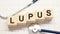 Lupus word written on wooden blocks and stethoscope on light white background