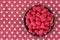 Luscious fresh picked raspberries in a large black ceramic bowl on a background of white stars on a field of red, top view