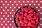 Luscious fresh picked raspberries in a large black ceramic bowl on a background of white stars on a field of red, top view