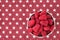 Luscious fresh picked raspberries in a white ceramic bowl on a background of white stars on a field of red, top view