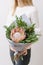 Lush bouquet of king Protea, eucalyptus and other greens. Young girl holding a flowers arrangements with various of