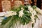 Lush floral arrangement of orchids and monstera leaves on wedding table. Wedding presidium in restaurant, copy space.