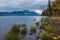 Lush lake coast overlooking snowcapped mountains.