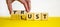 Lust or trust symbol. Businessman turns wooden cubes and changes the words `lust` to `trust`. Beautiful yellow table, white