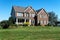 Luxurious brick house with a green lawn and trees at the entrance. Sunny summer day, cloudless sky