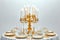 A luxurious candlelit dinner setting in a baroque style, an ornate golden candelabra holding white taper candles at its center.