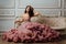 Luxurious girl in an evening cloudy dress sitting on a sofa in the studio interior.