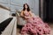 Luxurious girl in an evening cloudy dress sitting on a sofa in the studio interior.