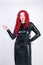 Luxurious plus size woman with Asian face, bright makeup and red curly hair posing in shiny closed long black dress on white backg