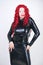 Luxurious plus size woman with Asian face, bright makeup and red curly hair posing in shiny closed long black dress on white backg