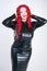 Luxurious plus size woman with Asian face, bright makeup and red curly hair posing in shiny closed long black dress on white backg