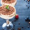Luxurious tiramisu in cocktail glasses decorated with cocoa powder on a dark background