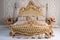 Luxury bedroom in light colors with golden furniture details. Big comfortable double royal bed in elegant classic