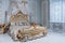 Luxury bedroom in light colors with golden furniture details. Big comfortable double royal bed in elegant classic