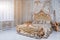 Luxury bedroom in light colors with golden furniture details. Big comfortable double royal bed in elegant classic