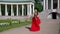 luxury blonde woman in red dress and red rose in hands is walking in garden of luxury palace