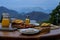 Luxury brunch meal on the table, meat, orange juice and fruits, mountains landscape in background