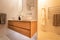 Luxury domestic bathroom shower and vanity with oak dresser drawers, twin basins, white color scheme and bright lighting