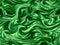 Luxury green silk fabric backgrounds. Metallic color of shiny textile, soft green texture. Satin folds, waves pattern.